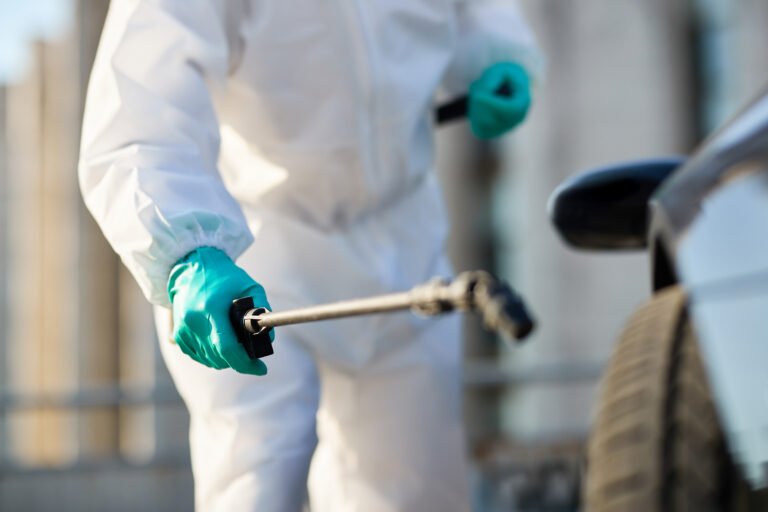 Close-up of man in protective suit disinfecting car tire during coronavirus epidemic.